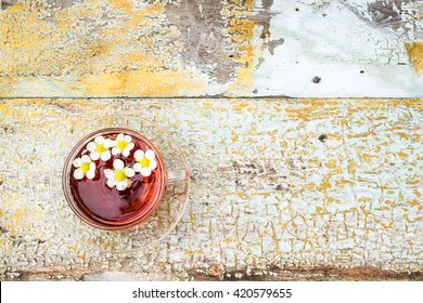 Glass cup of tea on old wooden surface. Small white flowers. - Powered by Shutterstock