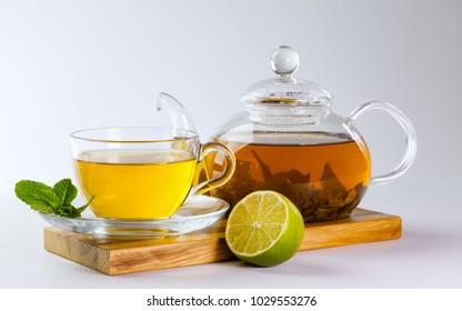 Glass cup and teapot of green tea, mint leaves and lime on a wooden board on a white background