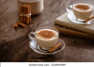 Glass cup of Turkish salep (milky traditional hot drink) with cinnamon sticks on dark wood