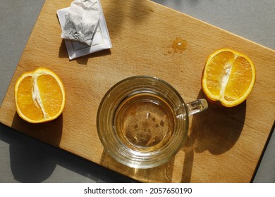 Glass Cup, Two Orange Slices, Tea Bag And Wooden Cutting Board On Gray Kitchen Background