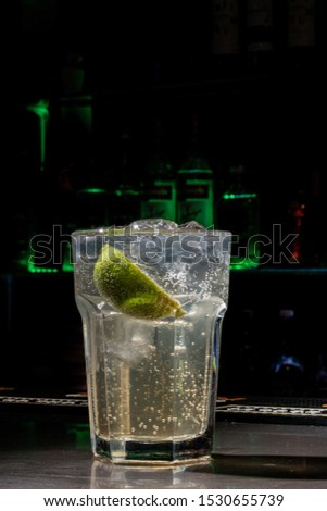 glass cup with vodka, slices of lemon and drink on black bar in the foreground with dark background