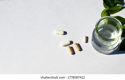 Glass cup with water and capsules and pilli on a white background. The topic of nutraceutical medicine and the intake of biological supplements. Copy space for text.