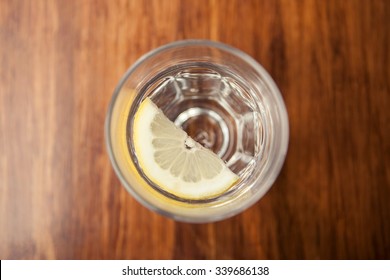 A Glass Cup Of Water With Half Healthy Lemon Top View On The Wood Table At The Daylight.