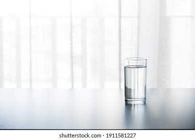 A glass cup of water on the table(desk), day light in the morning.