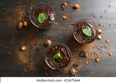 Glass Cups Of Chocolate Dessert With Fresh Mint And Hazelnuts On Black Wooden Table