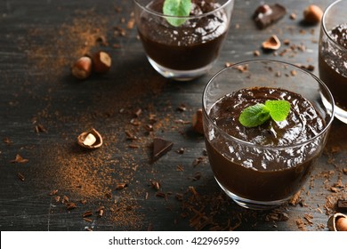 Glass Cups Of Chocolate Dessert With Fresh Mint And Hazelnuts On Black Wooden Table