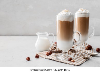 Glass cups of tasty latte and jug with milk on white background - Shutterstock ID 2110341641