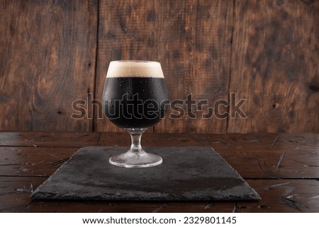 A glass of dark beer on a wood background. Beer on a slate tray. Serving stout beer. Front view.
