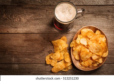 Glass Of Dark Beer With Potato Chips On A Wooden Background. Top View