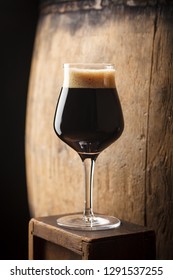 Glass Of Dark Stout Beer Standing Near An Old Wooden Barrel In A Cellar