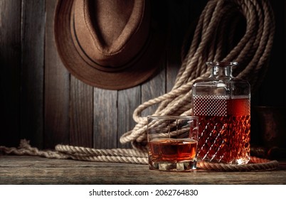 Glass And Decanter With Whiskey On An Old Wooden Table. In The Background Are A Hemp Rope And A Man's Hat.  Copy Space.