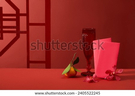 A glass decorated with a tangerine, small flowers and several red envelopes. Front view. Vacant space for product advertising