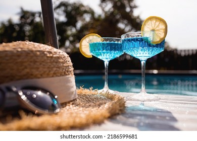 A glass of delicious blue cocktail "Blue Lagoon" and yellow lemons on the background of the pool. Alcoholic cocktail juicy fruit blue with curacao liqueur, ice cubes and a slice of lemon. 