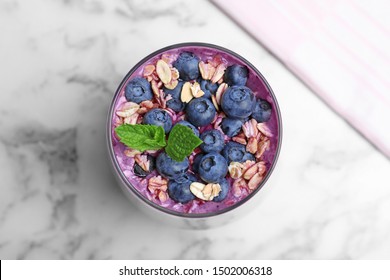 Glass Of Delicious Blueberry Smoothie With Granola And Mint On White Marble Table, Top View