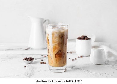 Glass of delicious cold brew with milk and coffee beans on white marble table - Shutterstock ID 2168051797
