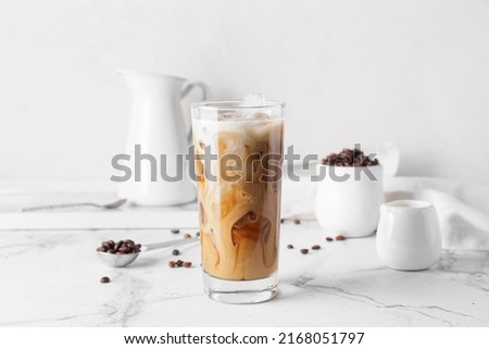 Glass of delicious cold brew with milk and coffee beans on white marble table