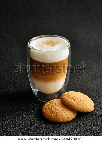 A glass of delicious latte and cookies on a black background. Delicious latte macchiato and cookies. Close-up