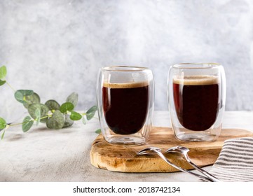 A glass double-sided cups of coffee with coffee in it on a wooden board on a grey background .