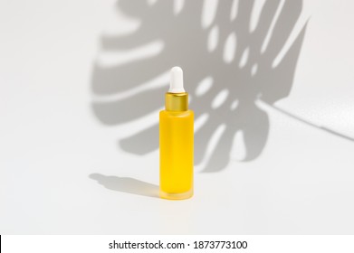 Glass Dropper Bottle Of Yellow Serum Or Essential Oil On White Background With Tropical Monstera Shadow. Organic Skin Care Cosmetics. Wellness, Spa And Beauty Treatment Concept. Product Mockup