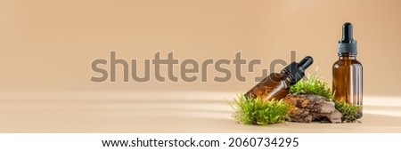Glass dropper bottles with cosmetic oil, essential or serum and green moss isolated on pastel beige background. Concept of natural organic spa cosmetics. Herbal homeopathic products Banner, copy space