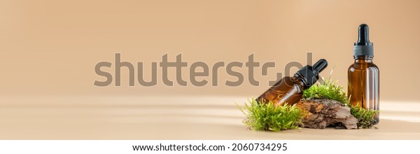 Glass dropper bottles with cosmetic oil, essential\
or serum and green moss isolated on pastel beige background.\
Concept of natural organic spa cosmetics. Herbal homeopathic\
products Banner, copy\
space