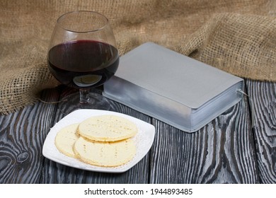 A glass of dry red wine and broken unleavened bread lie on a plate. To celebrate the Lord's Supper. Nearby lies the Bible. - Shutterstock ID 1944893485