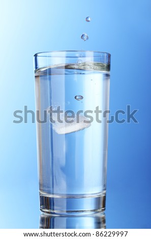 Glass with efervescent tablet in water on blue background Imagine de stoc © 