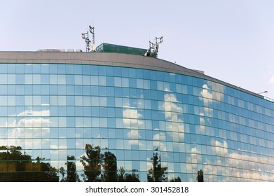 Glass Facade Of Office Building With Cell Tower, Satellite Dish And Sky Reflection