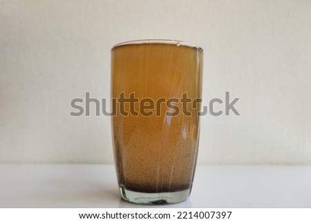 Glass filled with brown color bad, unhygienic, contaminated, undrinkable, impure, muddy and dirty drinking water isolated on white table background with copy space. Closeup side view. Impurity concept