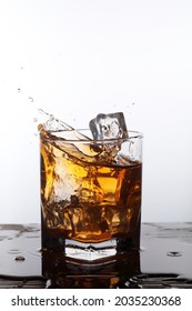 A Glass Filled With Liquor Like Amber Liquid Splashing As Ice Cubes Fall Into It.