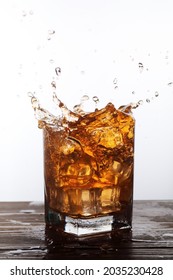 A Glass Filled With Liquor Like Amber Liquid Splashing As Ice Cubes Fall Into It.