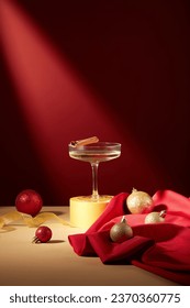 A glass filled with white wine and a cinnamon stick placed on yellow podium, displayed with baubles and red fabric. Another word for the Christmas season is Christmastime
