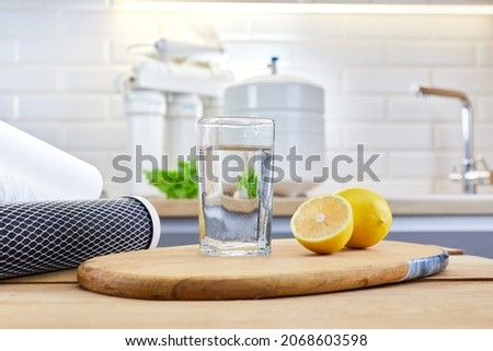 Glass of filtered clean water with reverse osmosis filter, lemons and cartridges on a table in kitchen. Concept Household filtration or purification system.
