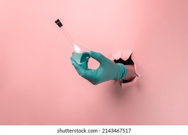 The glass flask with blue liquid in hand through a torn hole in the pink paper. - Shutterstock ID 2143467517