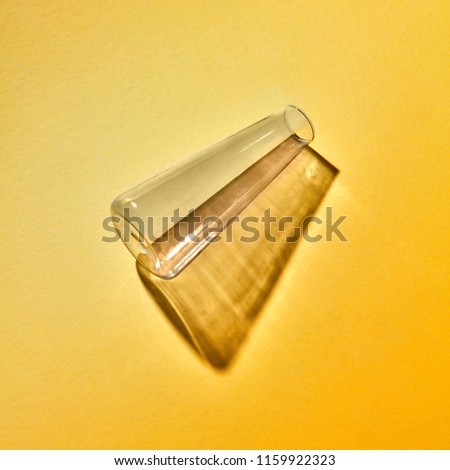 A glass flask empty with reflection and shadows lies on a yellow background, place for text. Laboratory tools for experiment. Laboratory concept.