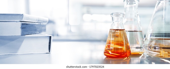 Glass Flask With Orange Solution And White Text Book In Chemistry Laboratory For Education Banner Background 