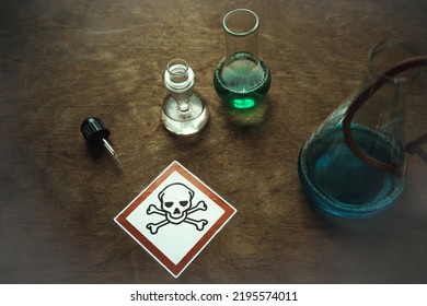 Glass flasks with a dangerous toxic substance on an old table. An emblem with a skull in a red square. Production of harmful substances. - Shutterstock ID 2195574011