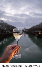 Glass of french sparkling white wine with bubbles champagne outdoor with view on green waters of Marne river and  lights of boulevard promenade in morning twilight, Epernay, Champagne, France - Shutterstock ID 2290174903