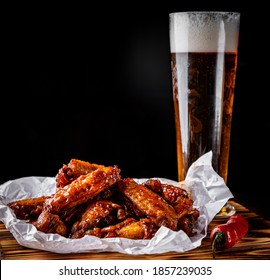 glass of fresh beer and fried chicken wings on wooden table on black background