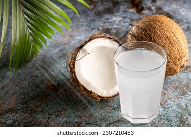 Glass with fresh coconut water and coconuts on the table.
