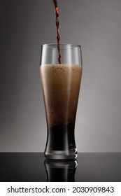 Glass Of Fresh And Cold Beer On A Gray Background. Detail Of Dark Beer With Overflowing Foam Head. Stream Of Dark Stout Pours Into A Beer Glass