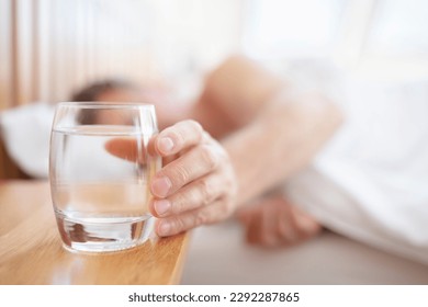 Glass of fresh drinking water on bed bedside table man thirsty reaching hand