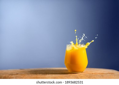 Glass of fresh orange juice splash on on wooden table and blue background. Dynamic pour of fruit juice in the morning. Space for text
