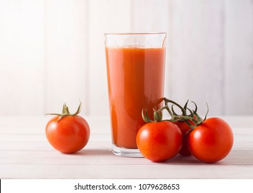 Glass of fresh organic tomato juice with raw tomatoes on light wooden background