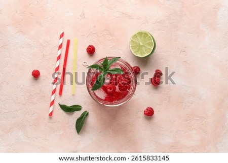 Glass of fresh raspberry lemonade with mint and lime on pink background
