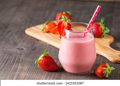 Glass of fresh strawberry milkshake, smoothie and fresh strawberries on pink, white and wooden background. Healthy food and drink concept.