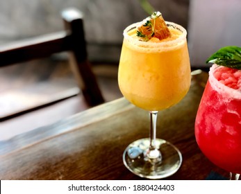 Glass of frosty orange frappe decorated by honeycomb and fresh thyme on wooden table with blurred watermelon rose slushy. Holidays food and drink, Refreshing time and enjoy summer theme. (copy space)