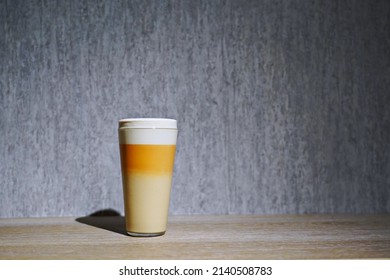 A Glass Of Frothy Drink Layered In Three Colors On A Wooden Countertop