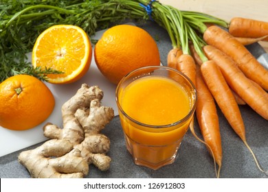 Glass of fruit juice with orange, carrots and ginger on a cutting board