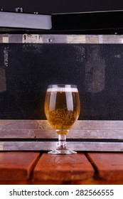 Glass Full Of Light Beer Standing On A Wooden Table With A Music Equipment Case In The Background